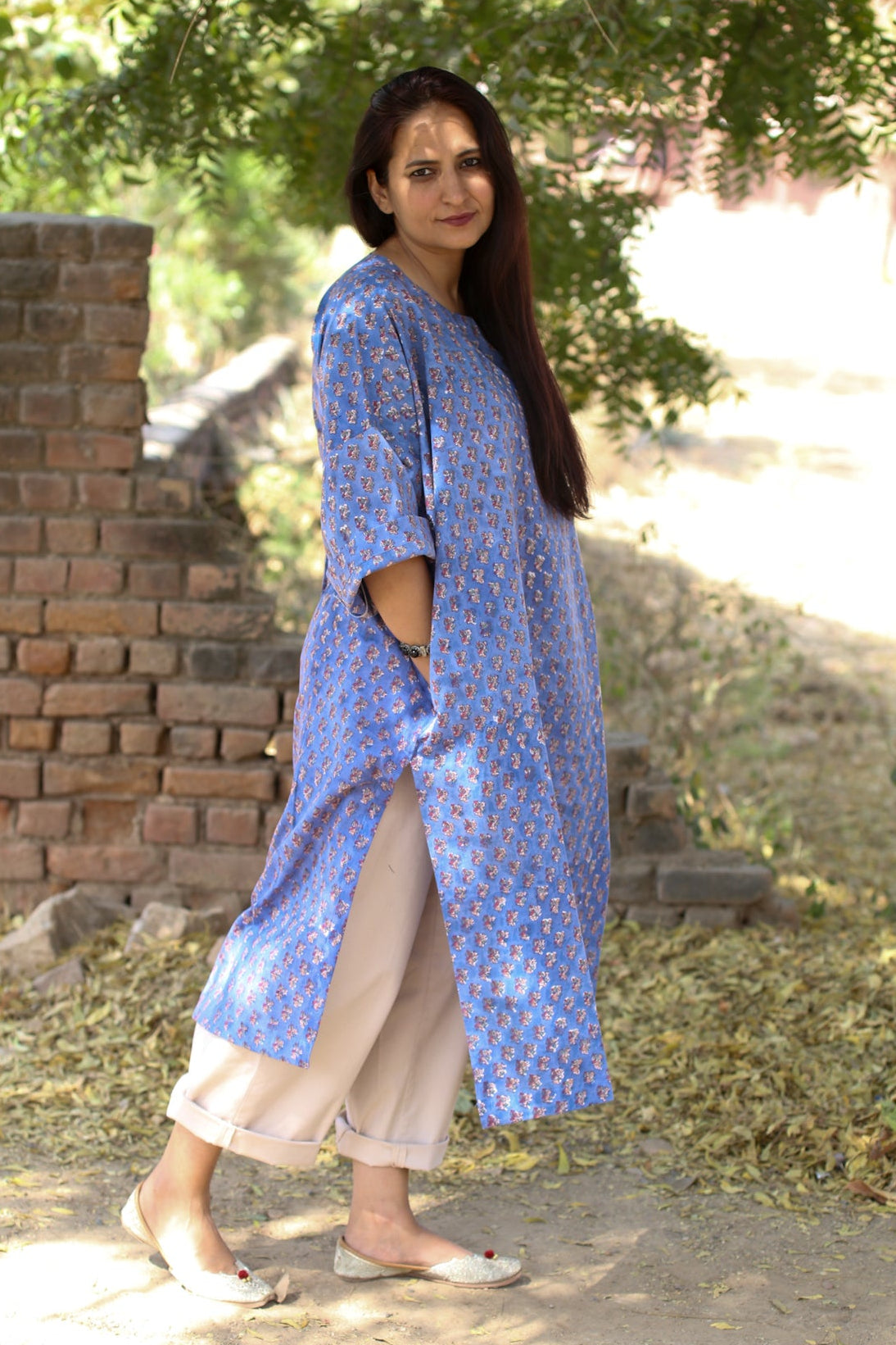 Woman wearing a blue patterned kurta with beige pants standing outdoors.