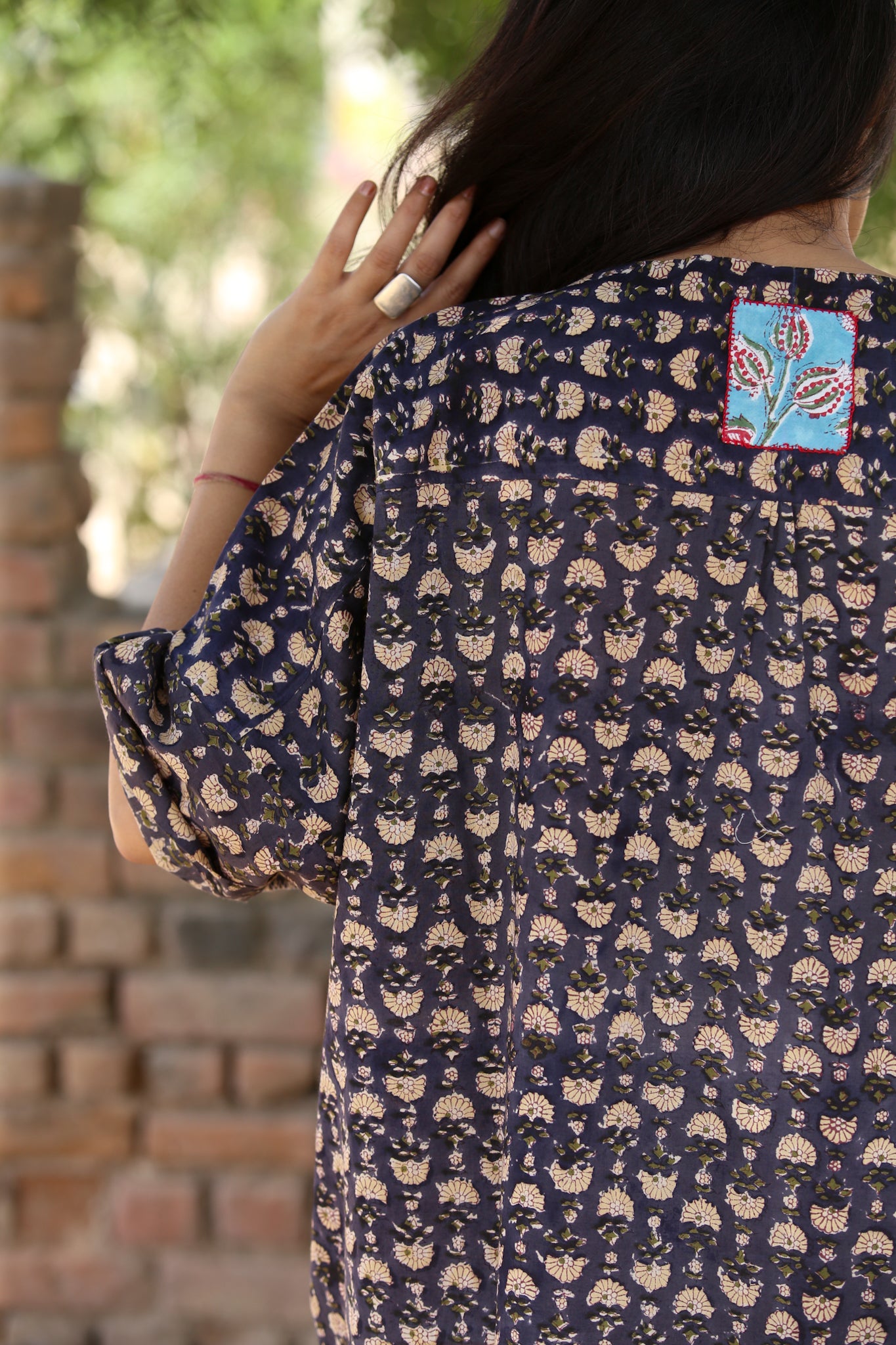 Person wearing a dark blue patterned dress with a colorful patch on a blurred outdoor background